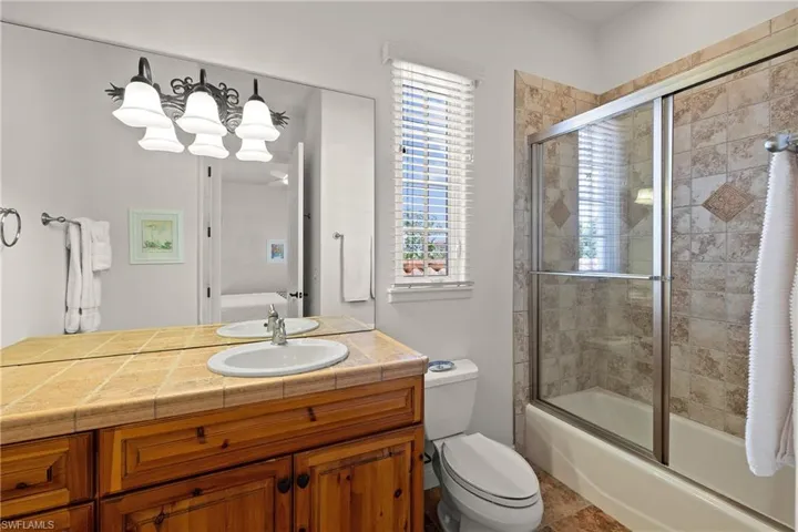 Full en suite bathroom with enclosed tub / shower combo, tile flooring, vanity, and toilet
