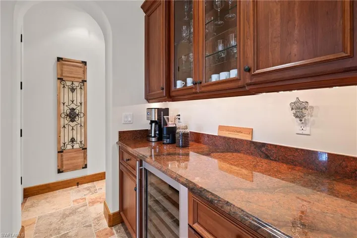 Bar featuring beverage cooler, dark stone countertops, and light tile floors