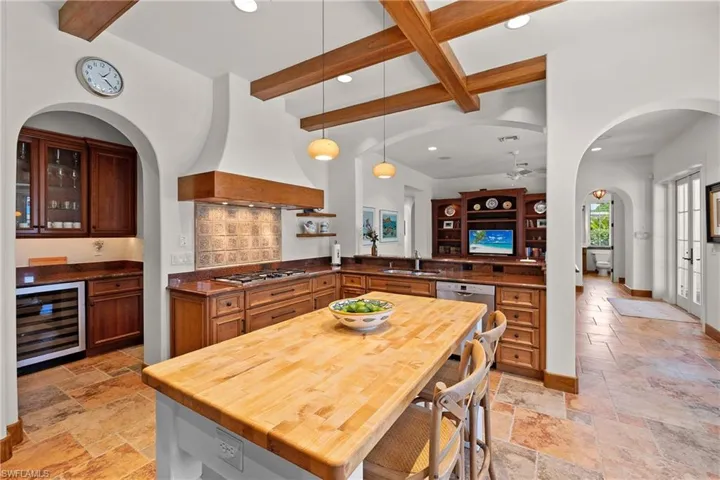 Kitchen with custom range hood, appliances with stainless steel finishes, beamed ceiling, beverage cooler, and sink
