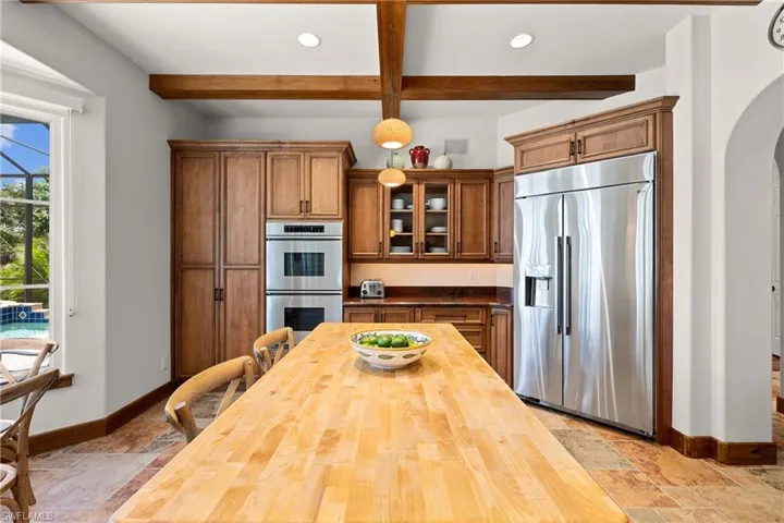 Kitchen featuring beam ceiling, appliances with stainless steel finishes, butcher block island, and light tile floors