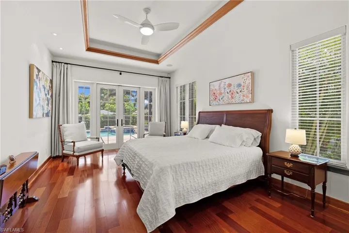 Primary Bedroom with access to outside, Minka ceiling fan, a raised ceiling, Brazilian Cherry wood flooring, and French doors