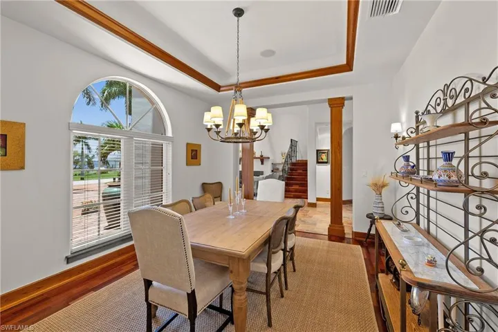 Dining area featuring a tray ceiling, Brazilian Cherry flooring, a chandelier, and decorative columns