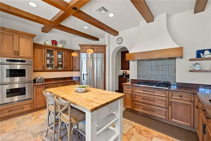 Kitchen with beamed ceiling, butcher block island, light tile floors, and stainless steel appliances