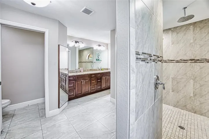 Bathroom featuring toilet, walk in shower, visible vents, and vanity