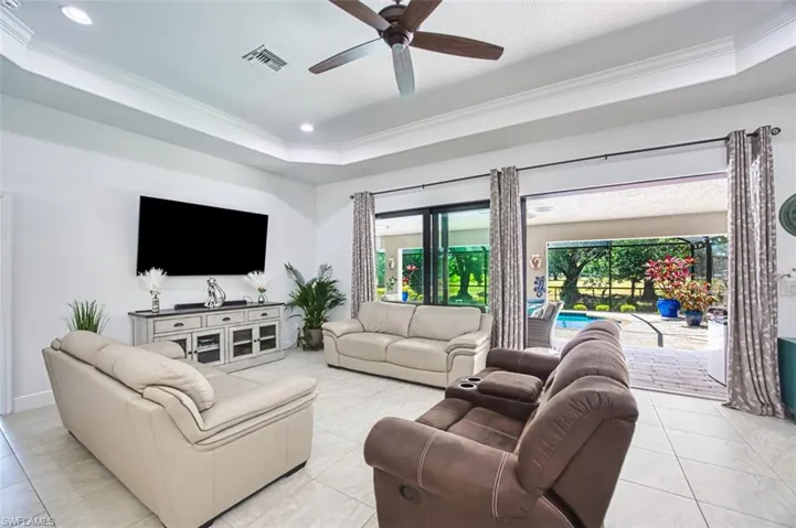 Living room featuring ceiling fan, visible vents, crown molding, light tile patterned floors, and a raised ceiling