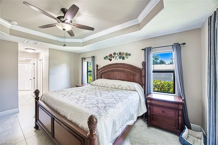 Bedroom with crown molding, visible vents, baseboards, ceiling fan, and a tray ceiling
