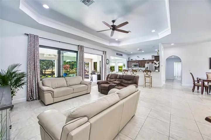 Living room featuring ceiling fan, a raised ceiling, arched walkways, a wealth of natural light, and visible vents