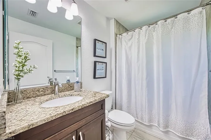 Full bath with vanity, shower / bath combination with curtain, toilet, and visible vents