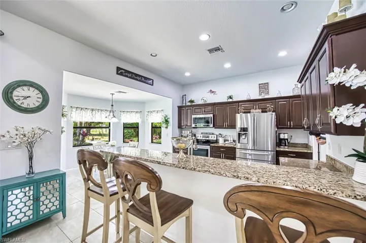 Kitchen with visible vents, dark brown cabinetry, a kitchen breakfast bar, light stone counters, and appliances with stainless steel finishes