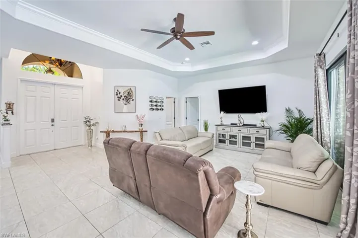 Living room with a ceiling fan, crown molding, a raised ceiling, baseboards, and recessed lighting