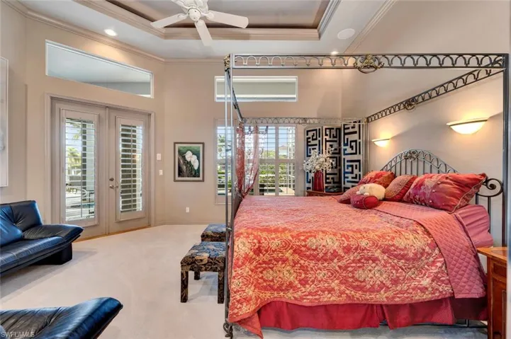 Carpeted primary bedroom featuring a tray ceiling, double glass doors with access to spa/lanai, two large walk-in closets, sitting area