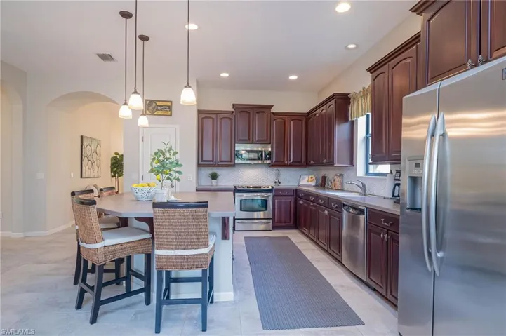 Kitchen with hanging light fixtures, a breakfast bar area, decorative backsplash, dark brown cabinets, and appliances with stainless steel finishes