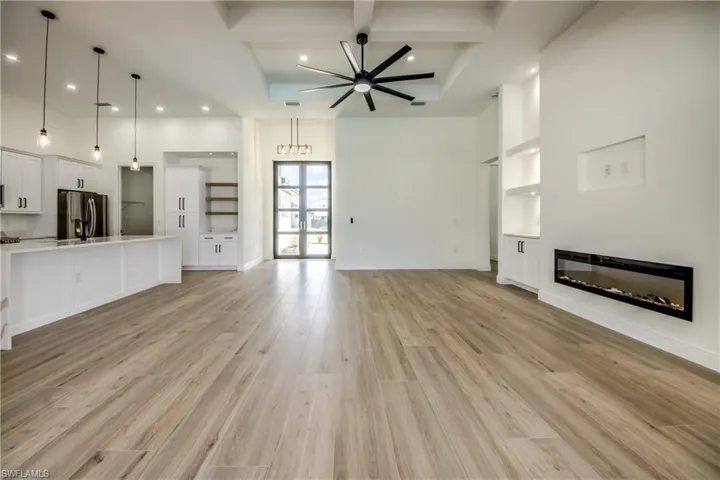 Unfurnished living room featuring beamed ceiling, coffered ceiling, light wood-style floors, ceiling fan, and a glass covered fireplace