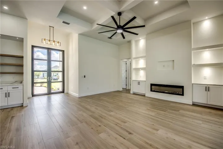 Unfurnished living room featuring french doors, coffered ceiling, light wood-type flooring, a glass covered fireplace, and beamed ceiling