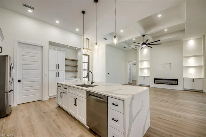 Kitchen featuring open floor plan, white cabinets, an island with sink, light stone countertops, and stainless steel appliances