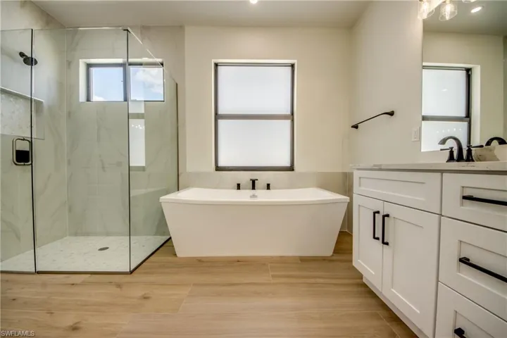 Full bathroom with vanity, a marble finish shower, a freestanding bath, and recessed lighting