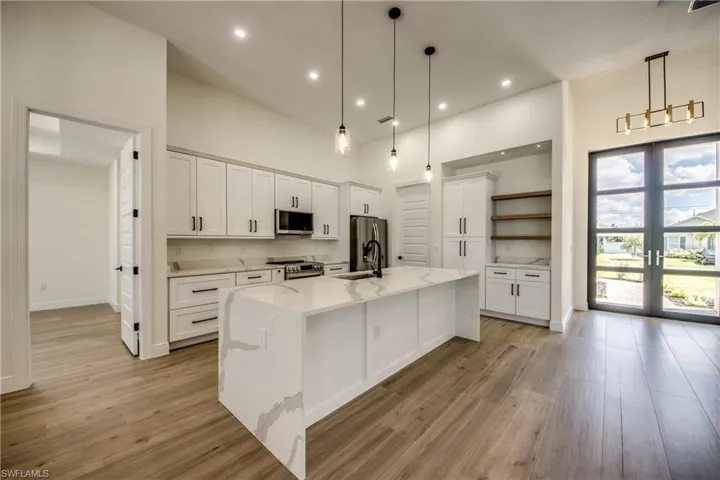 Kitchen featuring white cabinetry, open shelves, light stone counters, a kitchen island with sink, and stainless steel appliances