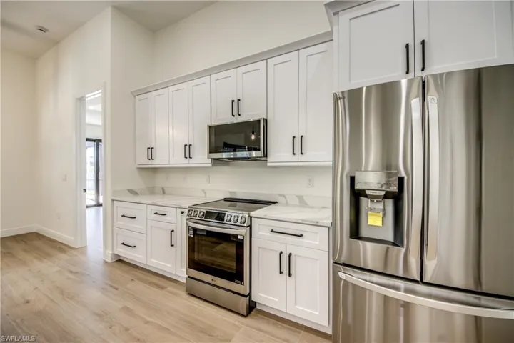 Kitchen featuring stainless steel appliances, white cabinets, light stone counters, and light wood-style flooring