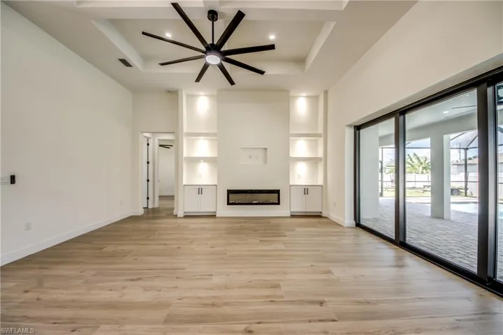 Unfurnished living room with light wood-style floors, a glass covered fireplace, a towering ceiling, a ceiling fan, and built in shelves