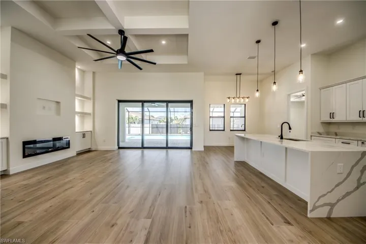 Living room with a ceiling fan, a glass covered fireplace, coffered ceiling, light wood-type flooring, and beamed ceiling