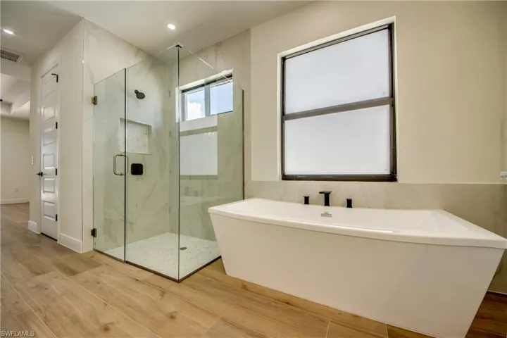 Full bathroom with wood finished floors, a freestanding tub, a marble finish shower, and recessed lighting