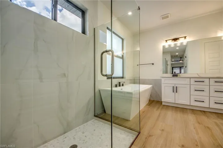 Bathroom featuring healthy amount of natural light, a freestanding tub, vanity, light wood-type flooring, and a wainscoted wall