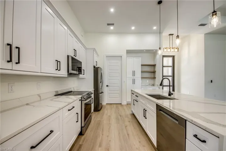 Kitchen with light stone counters, appliances with stainless steel finishes, light wood-style flooring, white cabinetry, and hanging light fixtures