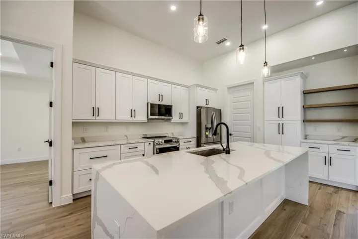 Kitchen featuring white cabinetry, light stone counters, open shelves, stainless steel appliances, and recessed lighting
