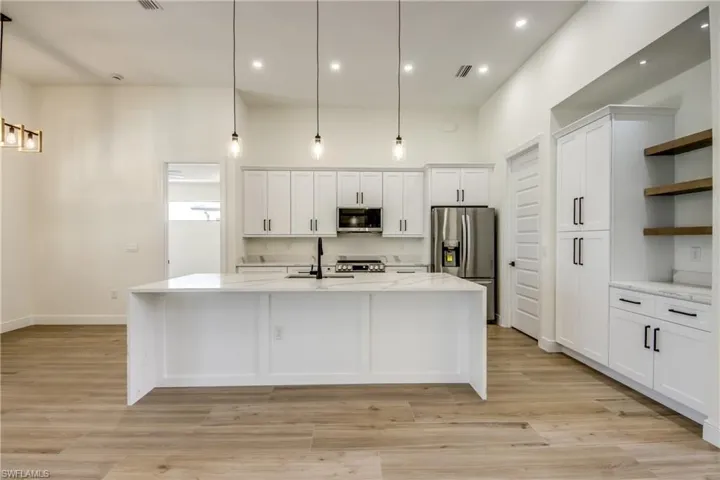 Kitchen with open shelves, white cabinets, light stone counters, stainless steel appliances, and recessed lighting