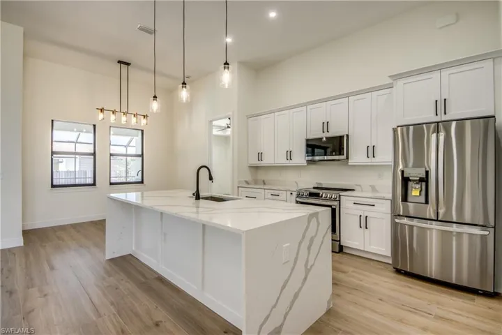 Kitchen with appliances with stainless steel finishes, light stone countertops, white cabinetry, and an island with sink