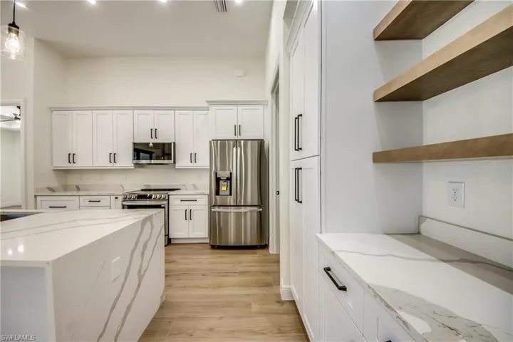 Kitchen with stainless steel appliances, light stone counters, and white cabinets