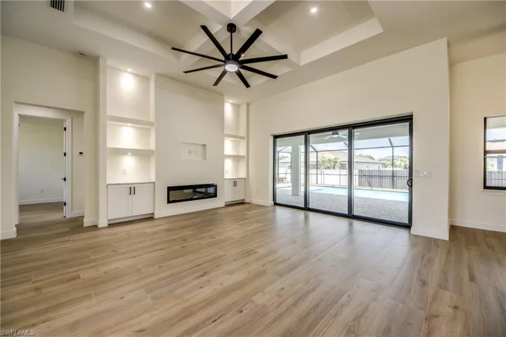 Unfurnished living room featuring built in shelves, coffered ceiling, light wood finished floors, beam ceiling, and a glass covered fireplace