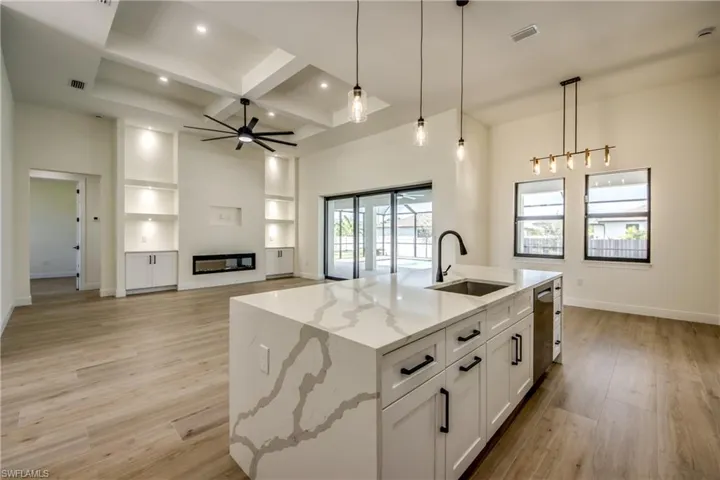 Kitchen with pendant lighting, light stone countertops, open floor plan, a glass covered fireplace, and light wood finished floors