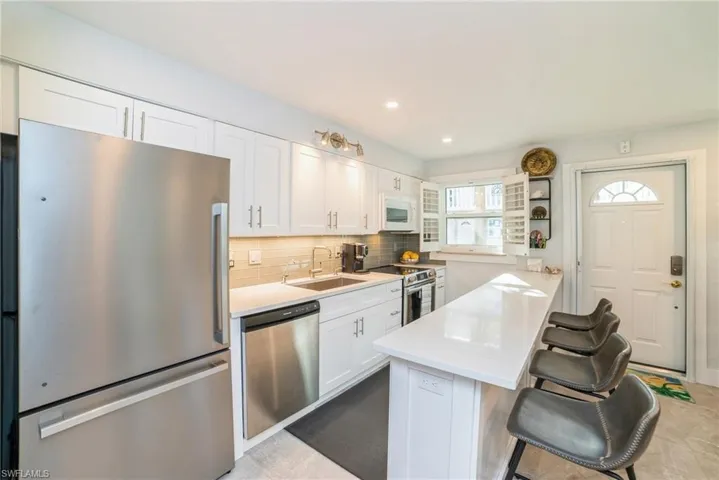Kitchen with appliances with stainless steel finishes, white cabinets, a breakfast bar area, backsplash, and a peninsula