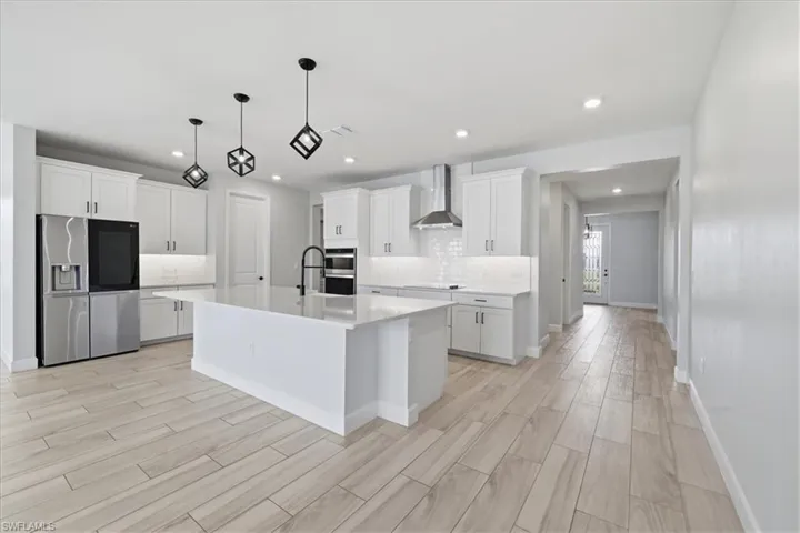 Kitchen featuring stainless steel appliances, decorative backsplash, white cabinets, and wood tiled floors