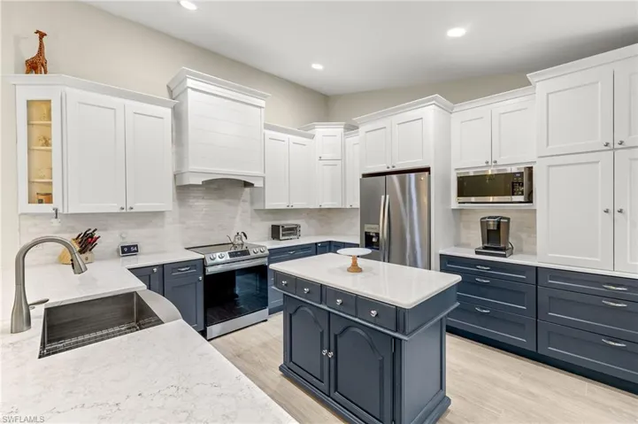 Kitchen with a farmhouse apron sink, custom exhaust hood, appliances with stainless steel finishes, and white and navy cabinetry.