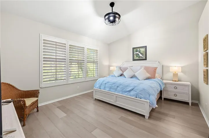 Bedroom with lofted ceiling, plantation shutters and light wood flooring