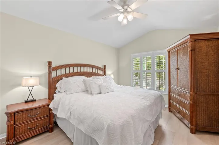 Inviting guest bedroom featuring vaulted ceiling, plantation shutters, wood floors.