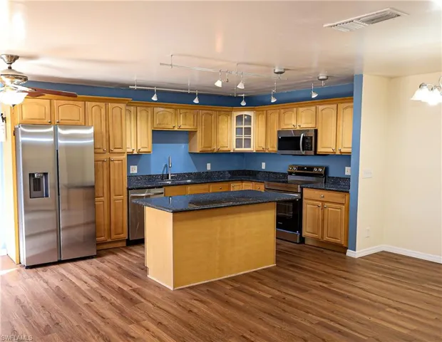 Kitchen featuring stainless steel appliances, dark stone countertops, dark wood-type flooring, and glass fronted cabinets