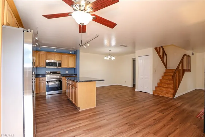 Kitchen featuring stainless steel appliances, ceiling fan, suspended lighting, light wood-type flooring, and open floor plan