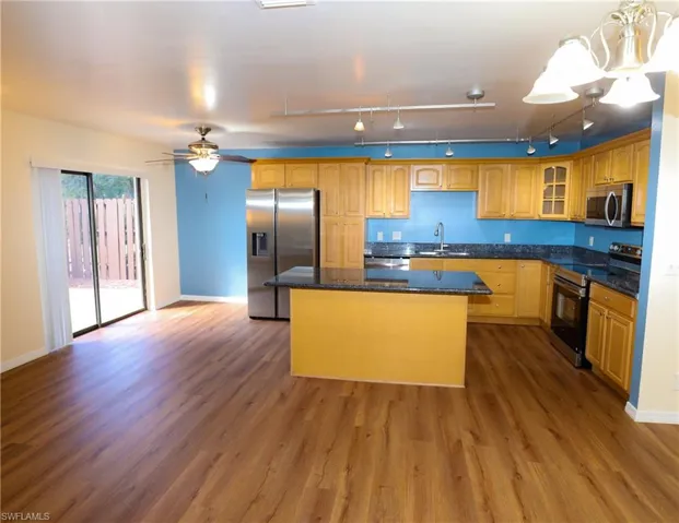 Kitchen featuring stainless steel appliances, a kitchen island, dark stone counters, glass insert cabinets, and track lighting