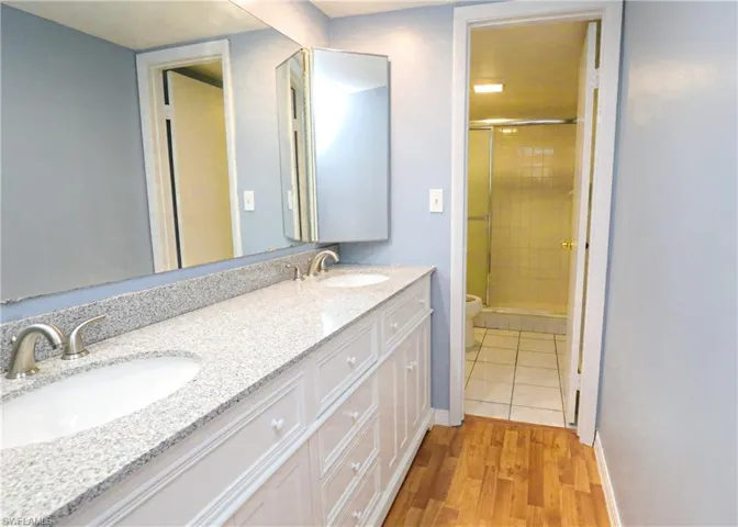 Bathroom featuring a stall shower, double vanity, and light wood finished floors