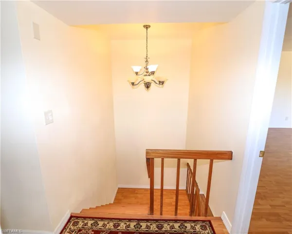 Stairway with wood finished floors and hanging lights