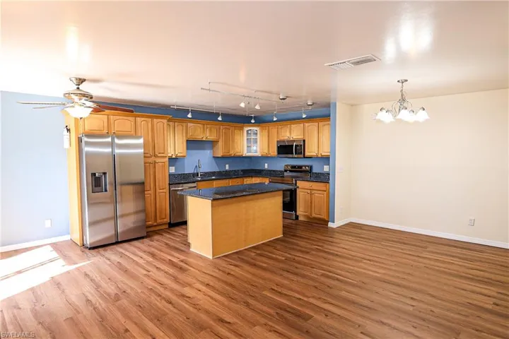 Kitchen featuring stainless steel appliances, glass fronted cabinets, a kitchen island, light wood-style floors, and suspended lighting