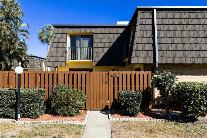 View of side of home featuring mansard roof, brick siding, and a gate