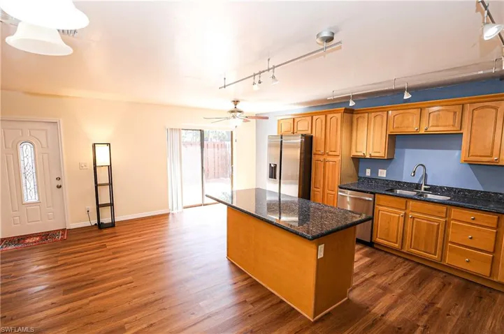 Kitchen with track lighting, wood finish cabinetry, dark stone countertops, stainless steel appliances, and a center island