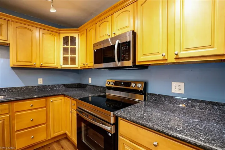 Kitchen featuring stainless steel appliances, glass insert cabinets, dark stone counters, and light wood finished floors