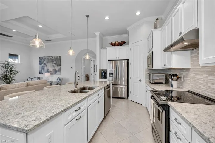 Kitchen featuring appliances with stainless steel finishes, arched walkways, crown molding, white cabinetry, and under cabinet range hood