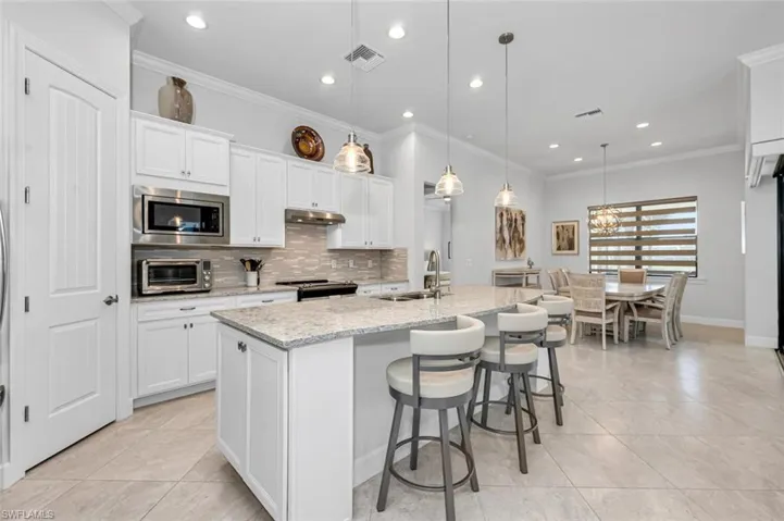 Kitchen featuring white cabinets, recessed lighting, ornamental molding, light stone countertops, and tasteful backsplash