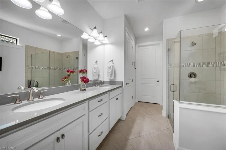 Full bath featuring double vanity, a shower stall, recessed lighting, and light tile patterned floors
